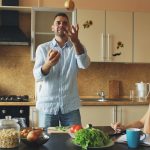 Attractive loving couple having fun in the kitchen. Handsome man juggle with apples to impress his girlfriend at home