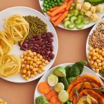 A vibrant mix of legumes, vegetables, nuts, and pasta arranged on white plates showcasing a balanced, healthy diet.